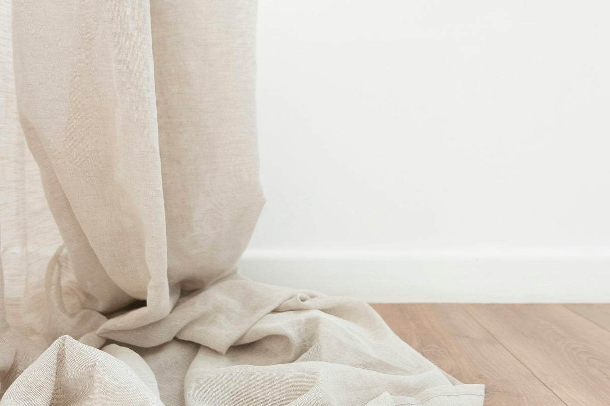 Sheer beige curtain pooling on a wooden floor